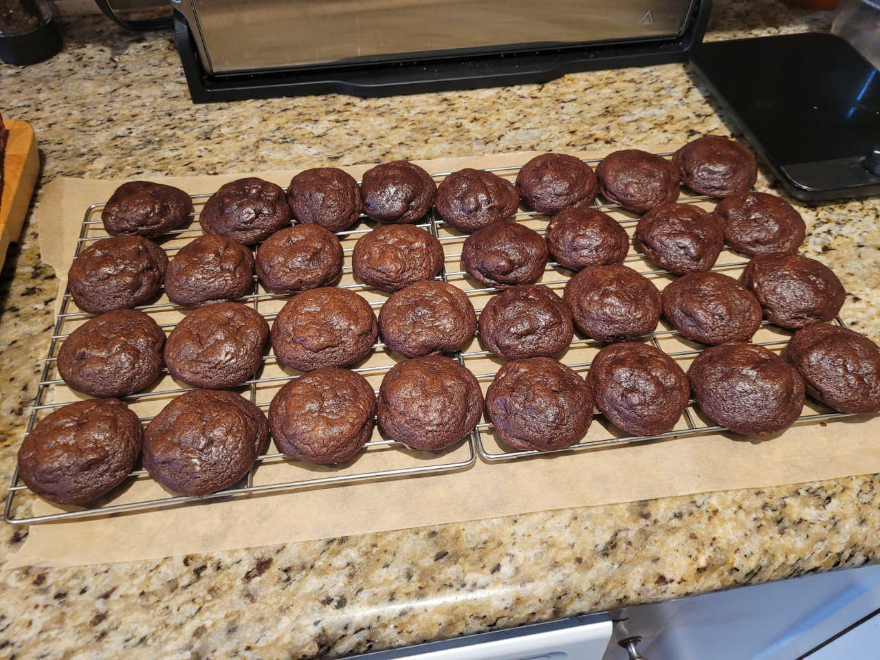 Picture of dozens of chocolate cookies on a cooling rack.