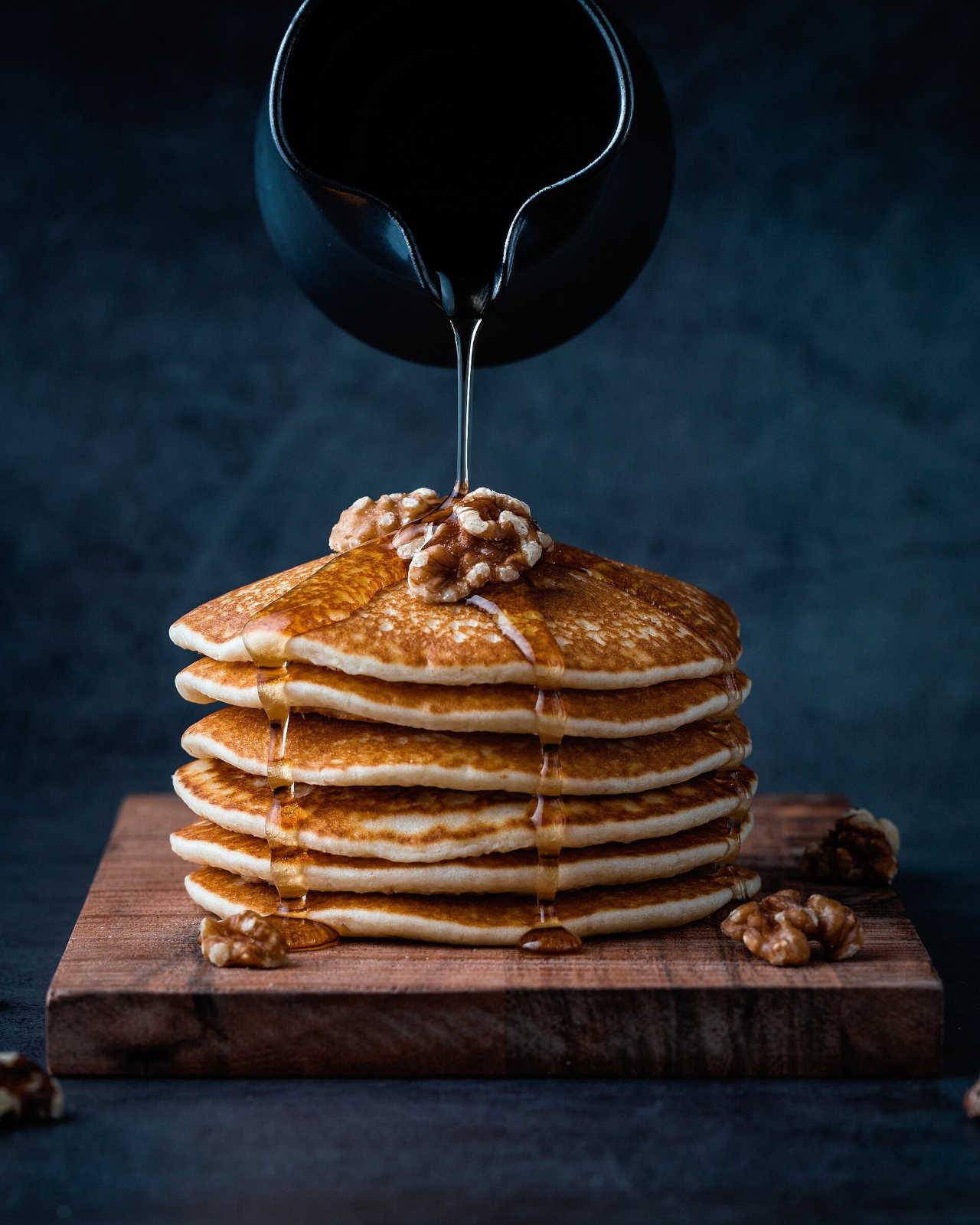 Picture of a stack of pancakes with honey being poured on it.